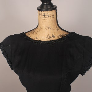 May include: A black sleeveless dress with a beaded neckline and a fitted silhouette.
