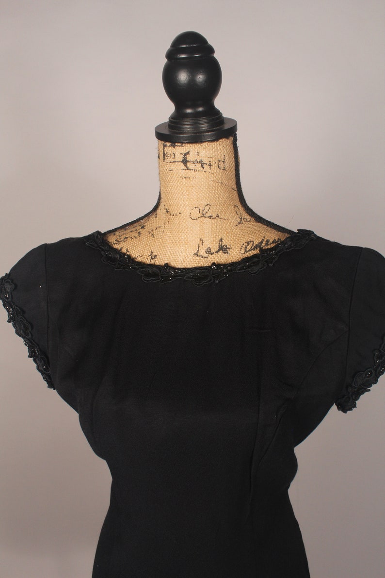 May include: A black sleeveless dress with a beaded neckline and a fitted silhouette.