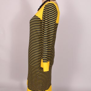 Puede incluir: Un vestido de rayas amarillas y negras con cuello redondo y mangas largas. El vestido tiene una banda amarilla en la parte superior e inferior.