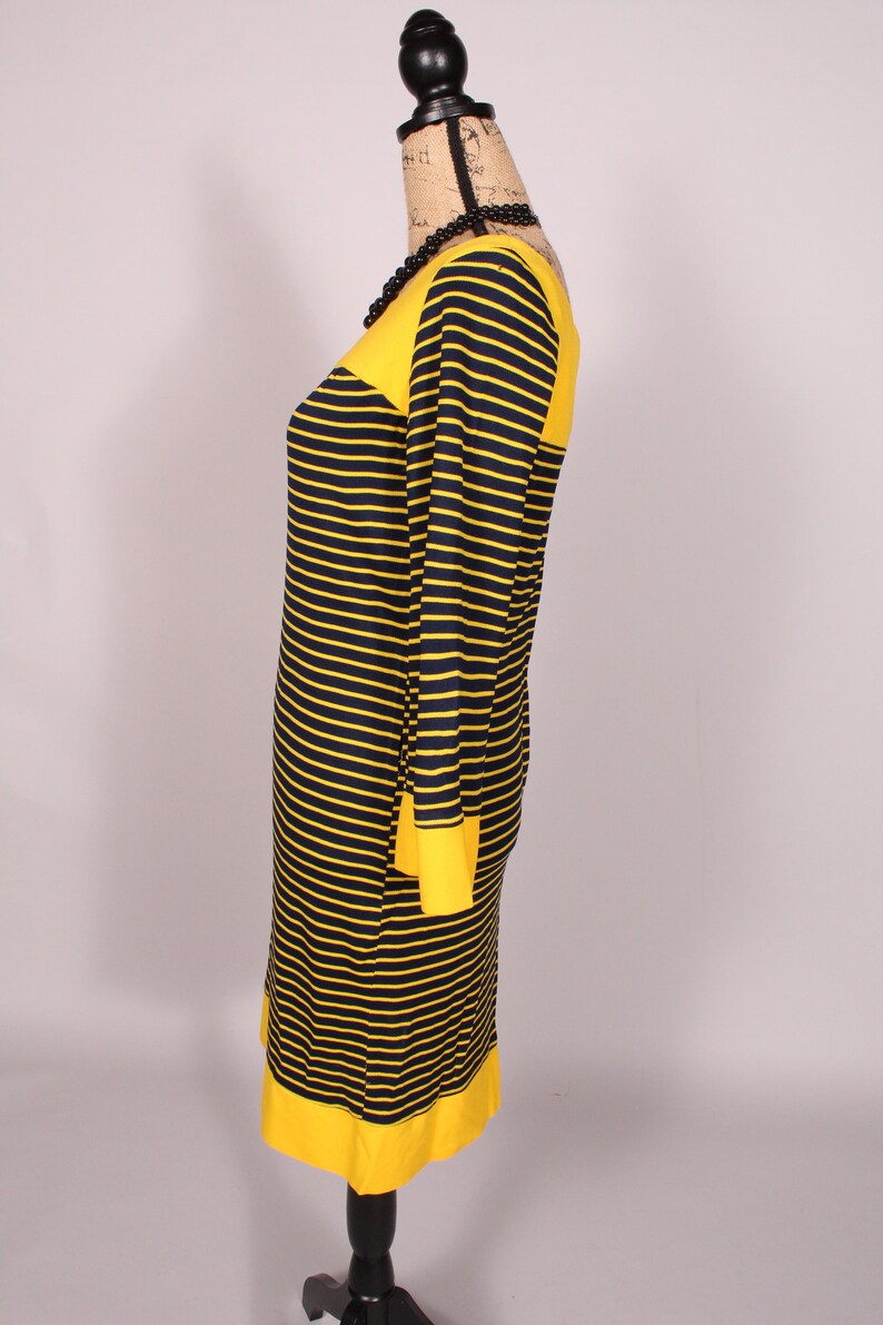 Puede incluir: Un vestido de rayas amarillas y negras con cuello redondo y mangas largas. El vestido tiene una banda amarilla en la parte superior e inferior.