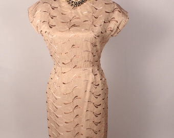May include: A beige dress with a brown abstract pattern. The dress has a scoop neckline and short sleeves. It is fitted through the bodice and flares slightly at the hem.