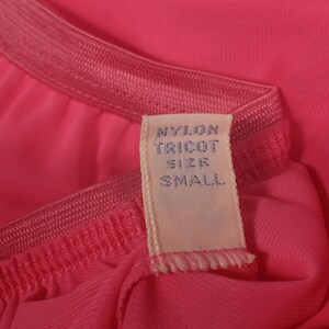 May include: A pink nylon tricot garment with a white tag that reads "Nylon Tricot Size Small".
