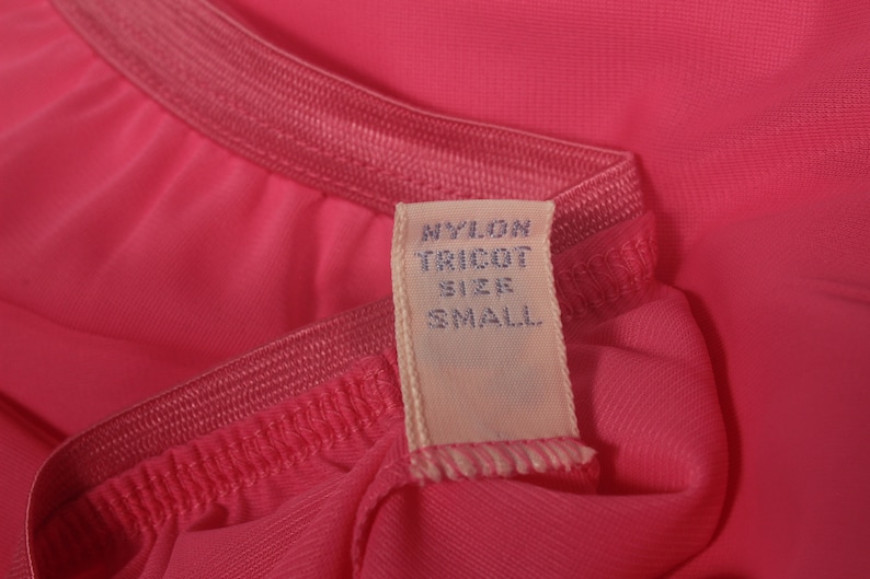May include: A pink nylon tricot garment with a white tag that reads "Nylon Tricot Size Small".