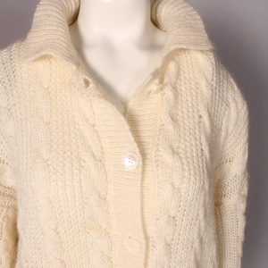 May include: A white knitted cardigan with a cable knit pattern and button closure.