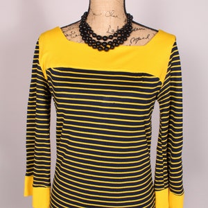 Puede incluir: Un vestido de rayas amarillas y negras con un escote amarillo y mangas largas. El vestido tiene un collar de cuentas negras.