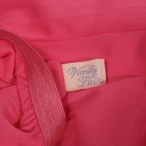 May include: A close-up of a pink fabric garment with a white label that says "Vanity Fair" in blue lettering.