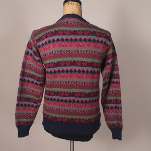 Puede incluir: Un su&eacute;ter de rayas multicolores con base azul marino. El su&eacute;ter tiene un patr&oacute;n de punto de trenza con acentos rosa, rojo, verde y azul.