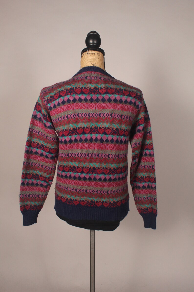 Puede incluir: Un su&eacute;ter de rayas multicolores con base azul marino. El su&eacute;ter tiene un patr&oacute;n de punto de trenza con acentos rosa, rojo, verde y azul.