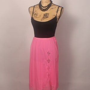 May include: A pink satin slip skirt with a lace trim and a diamond-shaped lace panel on the side.