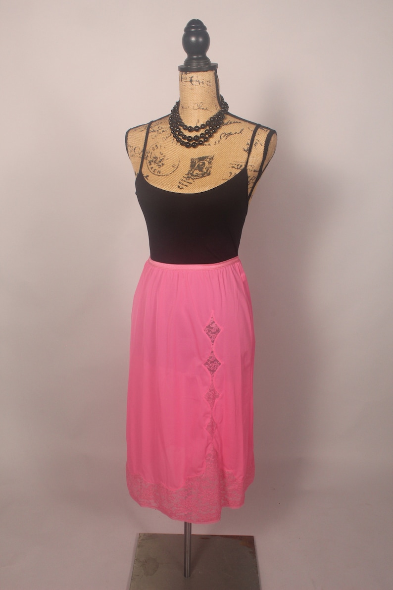 May include: A pink satin slip skirt with a lace trim and a diamond-shaped lace panel on the side.