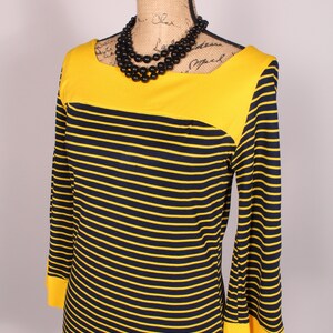 Puede incluir: Un vestido de rayas amarillas y negras con un escote amarillo y mangas largas. El vestido tiene un corpi&ntilde;o ajustado y una falda acampanada.