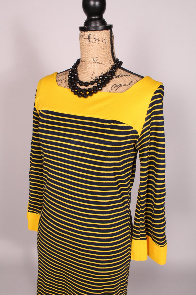 Puede incluir: Un vestido de rayas amarillas y negras con un escote amarillo y mangas largas. El vestido tiene un corpi&ntilde;o ajustado y una falda acampanada.