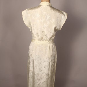 May include: A white sleeveless dress with a floral pattern. The dress has a fitted bodice and a flowing skirt. It is made of a silky material.