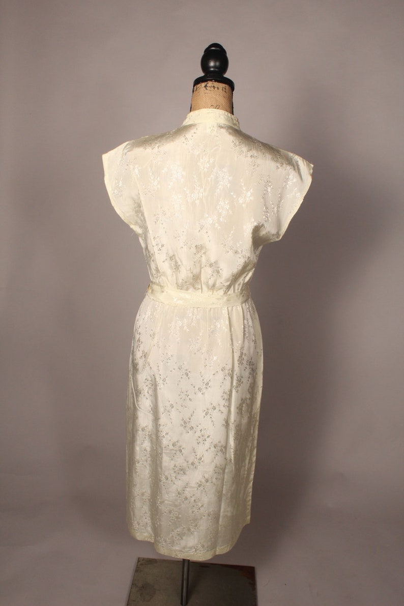 May include: A white sleeveless dress with a floral pattern. The dress has a fitted bodice and a flowing skirt. It is made of a silky material.