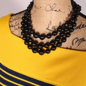 Puede incluir: Un collar de cuentas negras de tres hilos en un maniqu&iacute; de arpillera. El collar est&aacute; hecho de cuentas grandes y redondas.