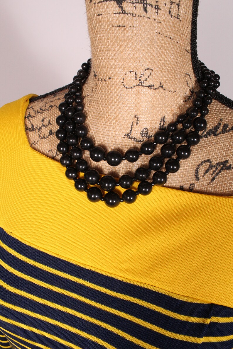 Puede incluir: Un collar de cuentas negras de tres hilos en un maniqu&iacute; de arpillera. El collar est&aacute; hecho de cuentas grandes y redondas.