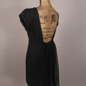May include: A black dress with a low back and a sheer overlay. The dress has a beaded trim along the neckline and back.