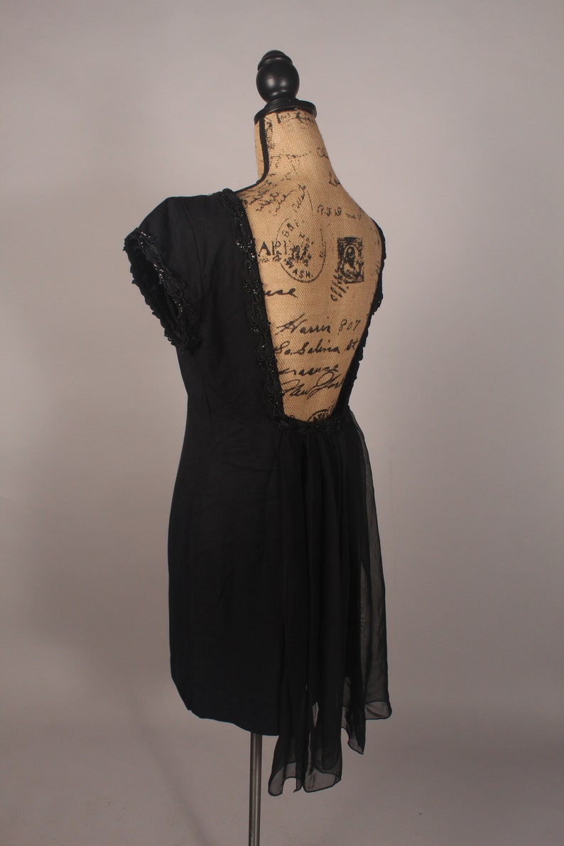 May include: A black dress with a low back and a sheer overlay. The dress has a beaded trim along the neckline and back.