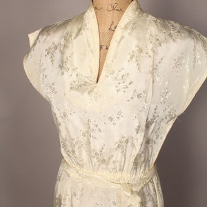 May include: A white silk dress with a floral pattern and a V-neckline. The dress has a sash tie at the waist.