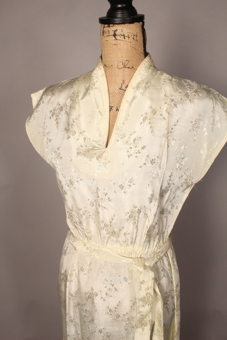 May include: A white silk dress with a floral pattern and a V-neckline. The dress has a sash tie at the waist.