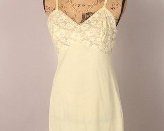 May include: A pale yellow slip dress with delicate lace trim at the neckline and hem. The dress is on a mannequin with a pearl necklace.