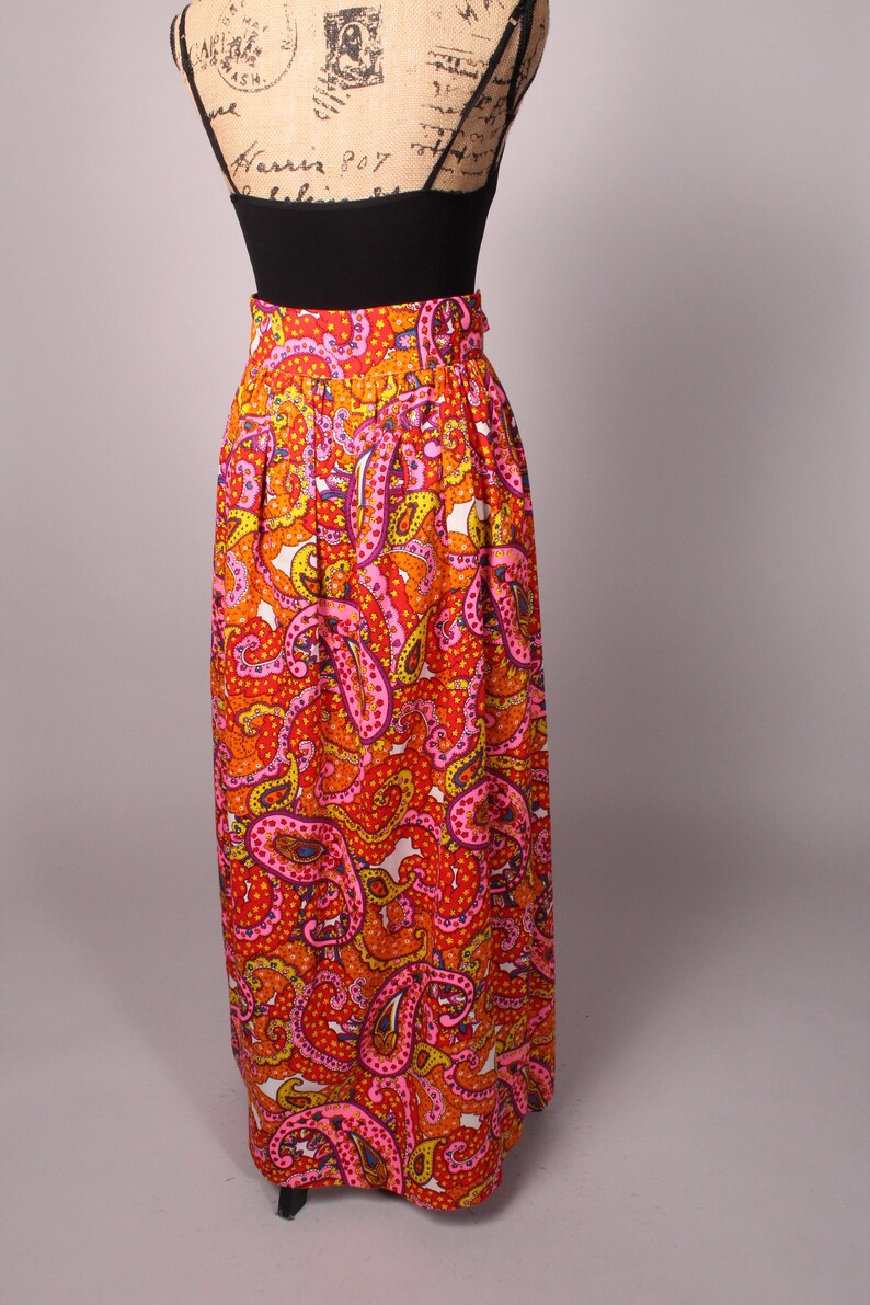 May include: A long, flowing skirt with a paisley print in shades of orange, pink, and yellow. The skirt has a high waist and a gathered design.