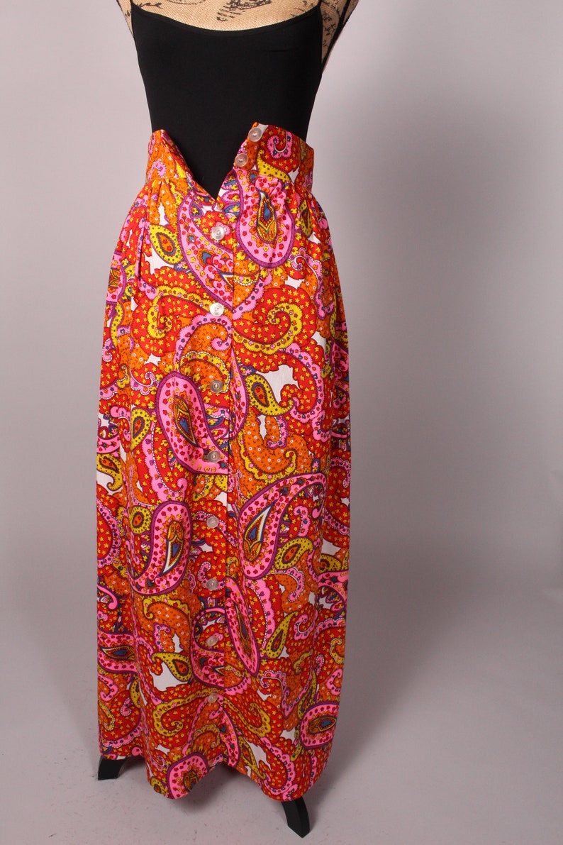 May include: A long, high-waisted skirt with a paisley print in shades of orange, pink, yellow, and white. The skirt has a button-up front and a fitted waistband.