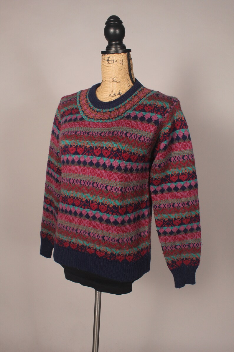 Puede incluir: Un su&eacute;ter a rayas de colores con un patr&oacute;n de coraz&oacute;n. El su&eacute;ter es azul marino, rosa, verde azulado y marr&oacute;n.