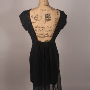 May include: A black sleeveless dress with a sheer overlay and a low back. The dress is on a dress form with a vintage-style pattern.