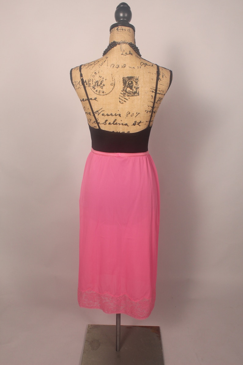 May include: A pink maxi slip skirt with a lace trim. The skirt is on a mannequin and is made of a silky material.