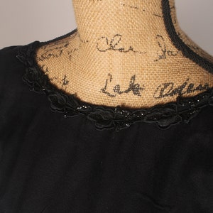 May include: A black dress with a lace trim around the neckline. The lace trim has small black beads.