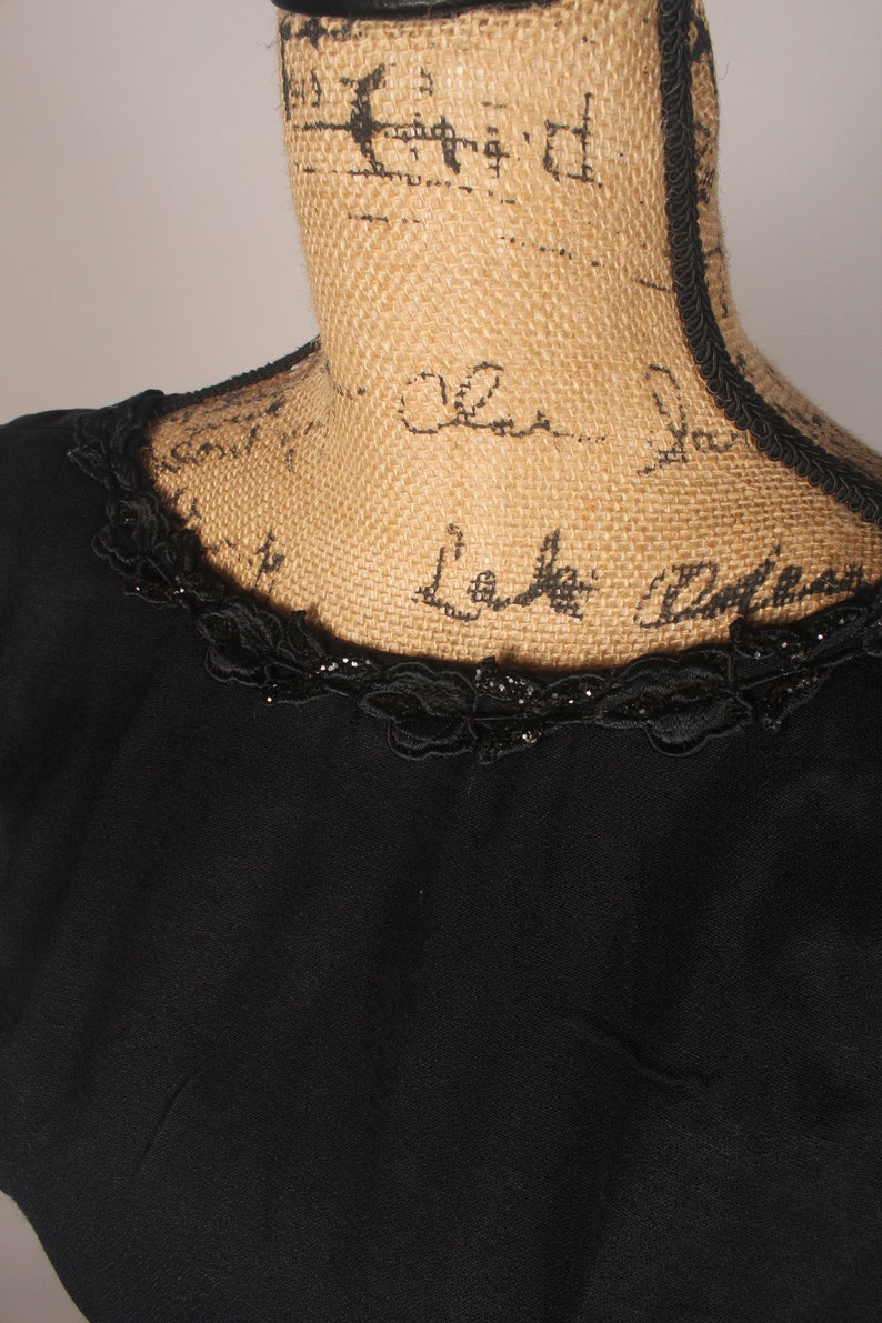 May include: A black dress with a lace trim around the neckline. The lace trim has small black beads.
