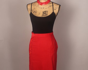 May include: A red pencil skirt with a button closure on the side. The skirt is on a mannequin wearing a black tank top and a red beaded necklace.
