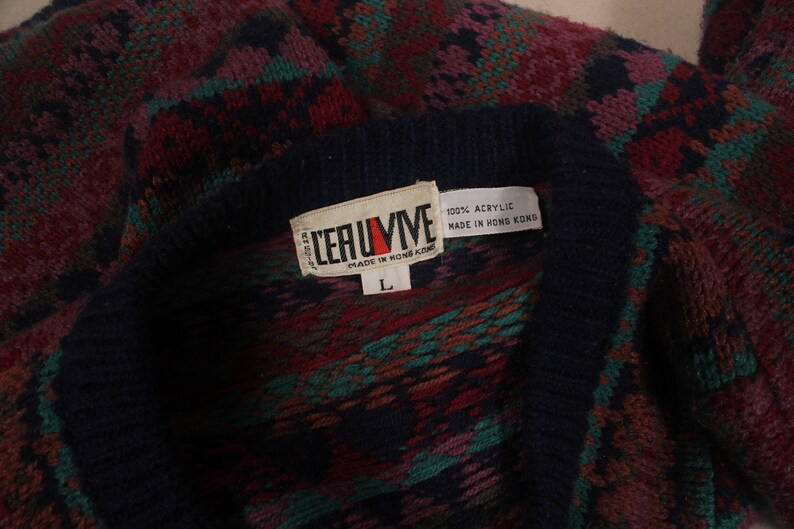 Puede incluir: Un su&eacute;ter de punto con estampado azul, rojo, verde y marr&oacute;n con una etiqueta blanca que dice "LERUIME" y "100% ACRYLIC MADE IN HONG KONG". La etiqueta tambi&eacute;n tiene una etiqueta de talla "L".