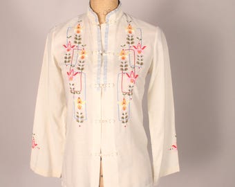 May include: A white button-up shirt with a mandarin collar and long sleeves. The shirt is embroidered with colorful flowers and geometric designs.