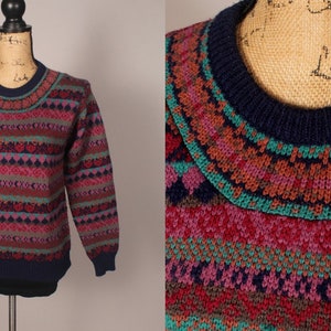 Puede incluir: Un su&eacute;ter azul marino con un patr&oacute;n geom&eacute;trico colorido. El patr&oacute;n incluye tonos de rosa, rojo, verde, marr&oacute;n y gris. El su&eacute;ter tiene cuello redondo.