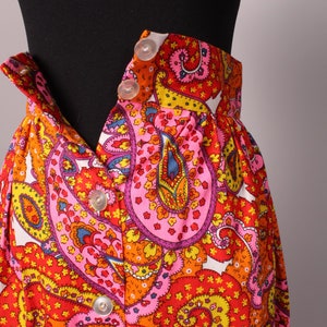 May include: A white skirt with a colorful paisley pattern in shades of pink, orange, yellow, and blue. The skirt has a button-up front closure.