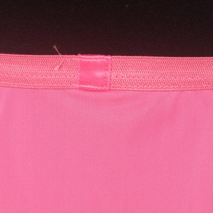 May include: Close-up of a pink fabric with a pink ribbon sewn across the top.