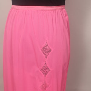 May include: A pink slip with a lace panel down the back. The lace is a diamond shape with scalloped edges.