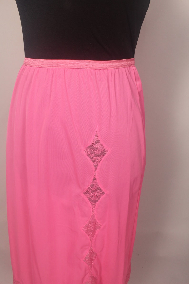 May include: A pink slip with a lace panel down the back. The lace is a diamond shape with scalloped edges.