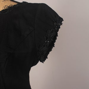 May include: Black sleeveless dress with a lace trim on the neckline and sleeves. The lace is a floral design with small black beads.