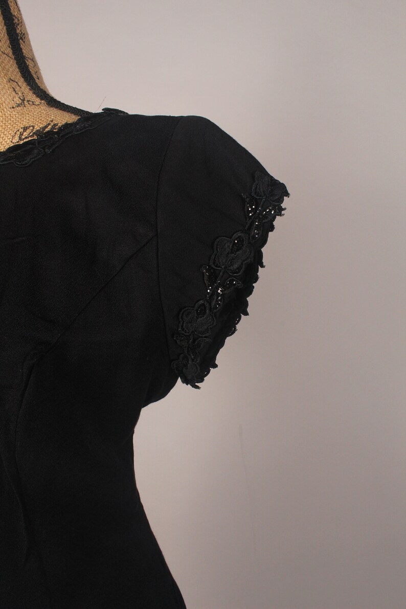 May include: Black sleeveless dress with a lace trim on the neckline and sleeves. The lace is a floral design with small black beads.