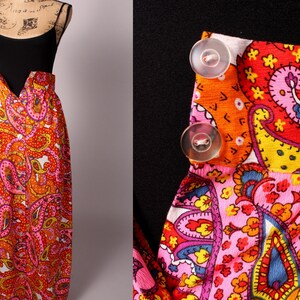 May include: A long, flowing skirt with a paisley print in shades of pink, orange, and yellow. The skirt has a black top and buttons down the front.