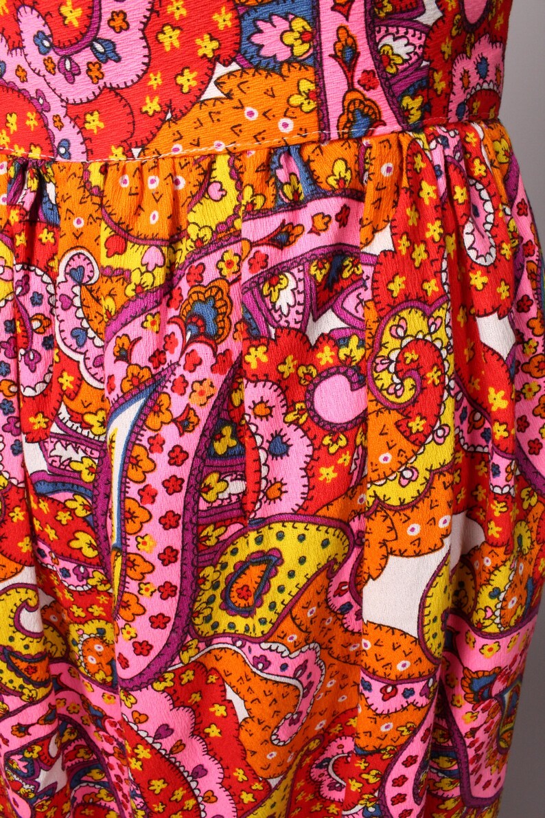 May include: A pink, orange, yellow, and red paisley print fabric with a white background. The fabric has a textured surface and is made of a soft, comfortable material.