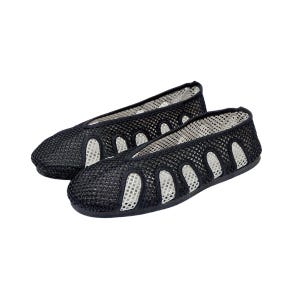 May include: A pair of black mesh flats with a rounded toe. The shoes have a breathable design with oval cutouts along the sides. The interior lining is white, providing contrast to the black exterior. The shoes are designed for comfort and style.