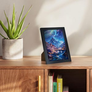 Puede incluir: Una impresi&oacute;n art&iacute;stica enmarcada en negro que representa un paisaje de fantas&iacute;a con un cielo estrellado, monta&ntilde;as y una ciudad con edificios iluminados. La impresi&oacute;n se exhibe sobre una superficie de madera.
