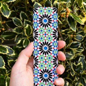 Peut inclure: Un marque-page rectangulaire présentant un motif géométrique répétitif avec des couleurs noir, blanc, rouge, vert et bleu. Le design se compose de motifs en forme d'étoile complexes et de formes imbriquées, créant un visuel détaillé.