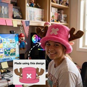 Könnte beinhalten: Ein rosa Plüschhut mit braunen Geweihen und einem weißen Kreuzemblem, inspiriert von der Anime-Figur Tony Tony Chopper aus One Piece. Das Bild enthält eine Zeichnung des Hutes mit dem Text "Made using this design."