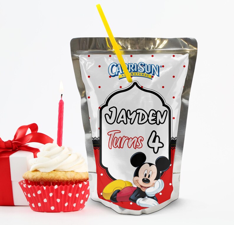 May include: A Capri Sun juice pouch with a yellow straw, featuring a Mickey Mouse design and the text "JAYDEN Turns 4". A cupcake with white frosting and a red candle is next to the juice pouch. A wrapped gift box with a red bow is also in the image.