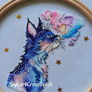 Könnte beinhalten: Kreuzstich-Stickerei eines Fuchses mit Galaxien-Design in Blau-, Lila- und Rosatönen. Der Fuchs ist in einem hölzernen Stickrahmen mit goldenen Sternverzierungen eingerahmt. Der Text "SkyLarkCrossStitch" ist sichtbar.